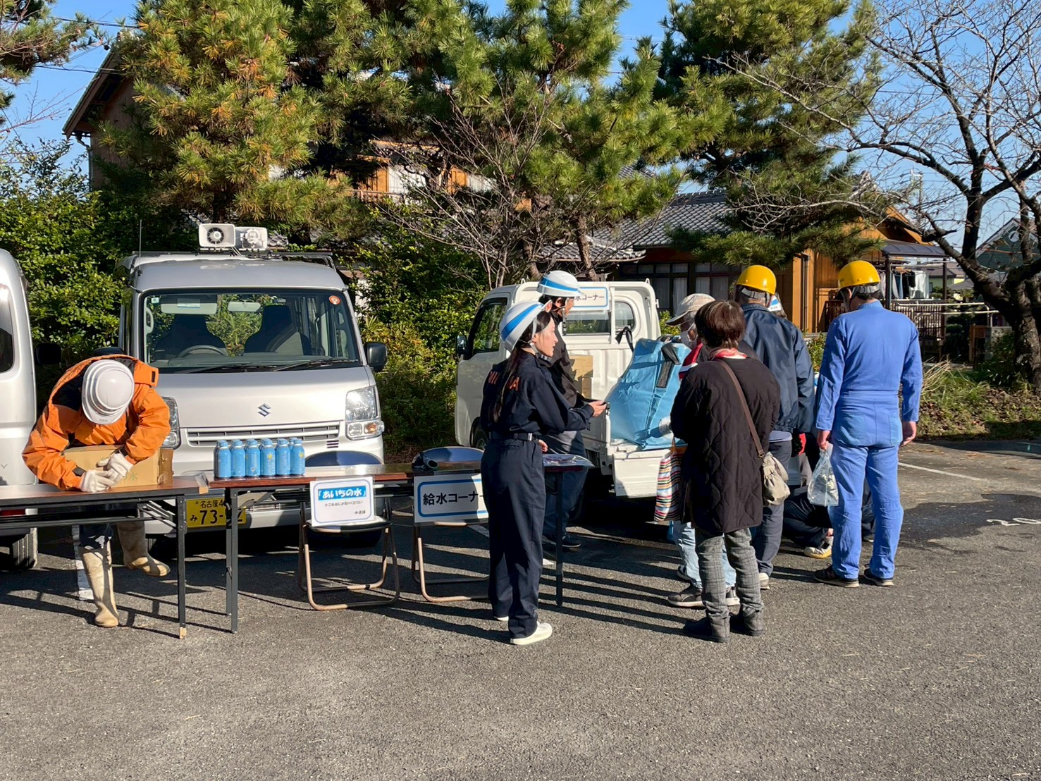 給水訓練コーナーで水道課職員の説明を受ける地元区住民。トラックに積んだ給水タンクから、非常用飲料用水袋に水を汲んでいる。