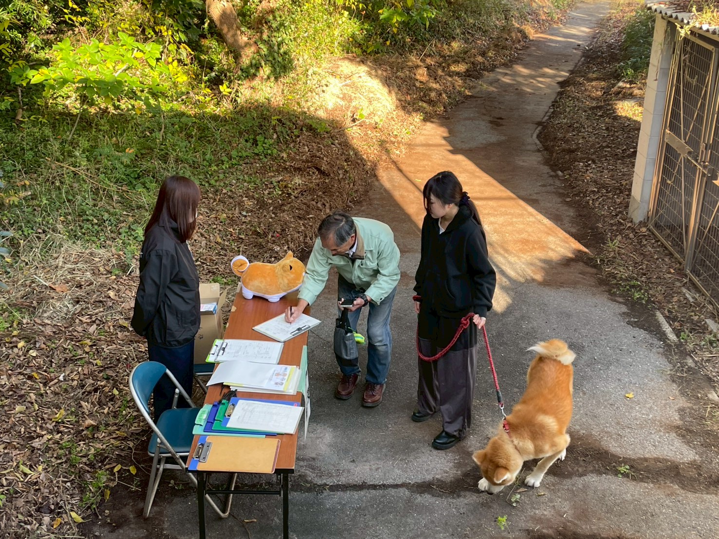 ペット避難訓練受付で用紙に記入する2人組の家族。リードにつながれた柴犬を連れている。