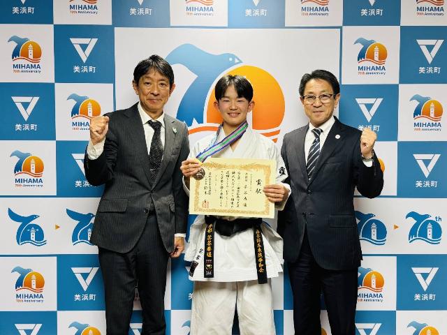 メダルと賞状を持つ茶谷泰遥さんと、町長と教育長がガッツポーズをしている様子。