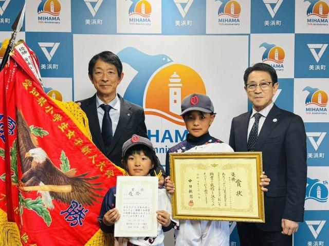 賞状を持つ大矢ひよりさんと大矢はぐみさん、優勝旗を広げる町長および教育長が写っている様子