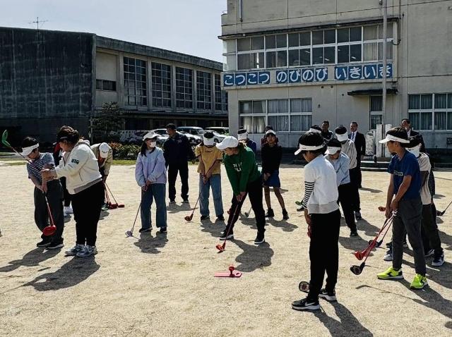 奥田小学校にて開催されたスナッグゴルフ教室で、児童がプロにクラブの握り方や振り方を教わっている様子。