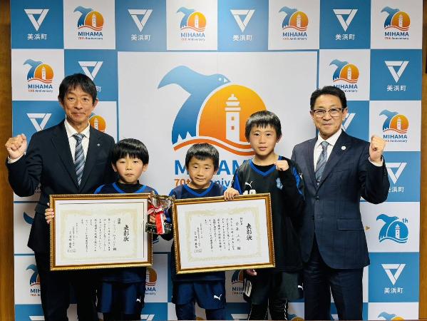 表敬訪問をした齋藤芳樹さん、齋藤汰樹さん、服部利翔さんが賞状を持ち、町長と教育長がガッツポーズをしている様子。