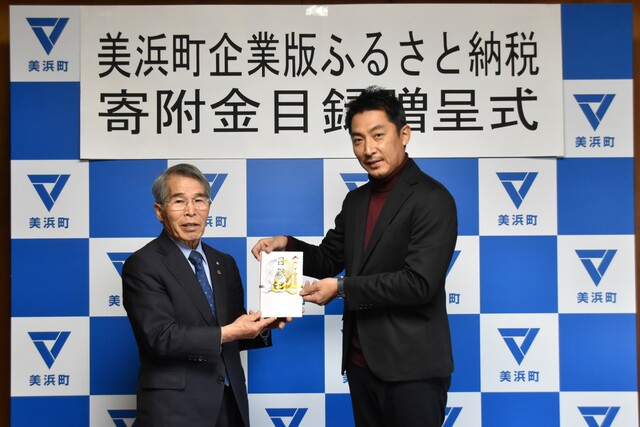 スーツを着た男性二人が寄付金を持って記念撮影している写真
