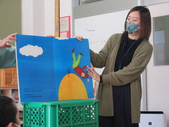国際交流員リム・イーシェンさんが大きめの絵本を台に置き読んでいる写真