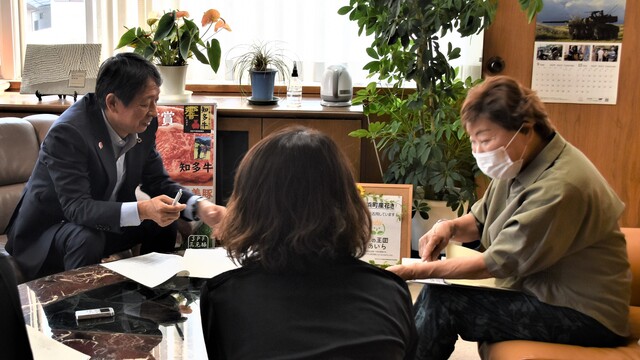 机に資料を置いて町長と女性が対話し、傍で女性が見守っている「町長対話室」の写真