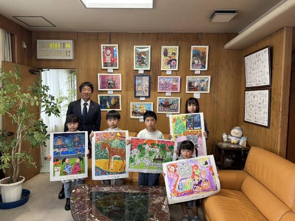 町長室にて、受賞した作品を持つ5人の受賞者と町長の様子。