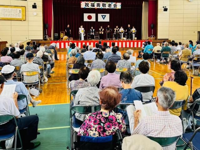 布土区の敬老会で、壇上でのパフォーマンスを参加者が見ている様子。