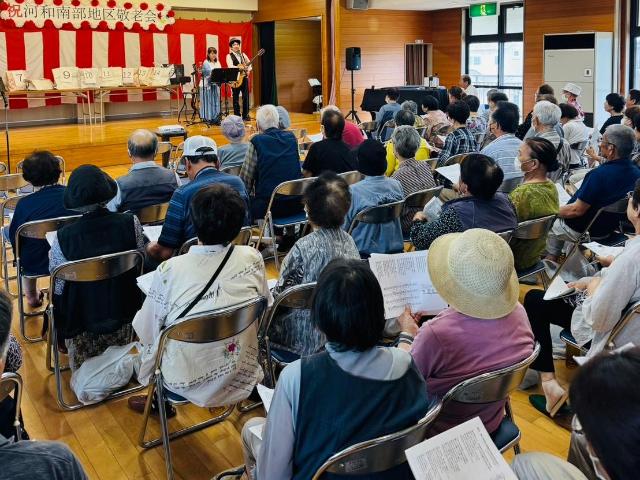 河和南部地区の敬老会で、壇上でのパフォーマンスを参加者が見ている様子。