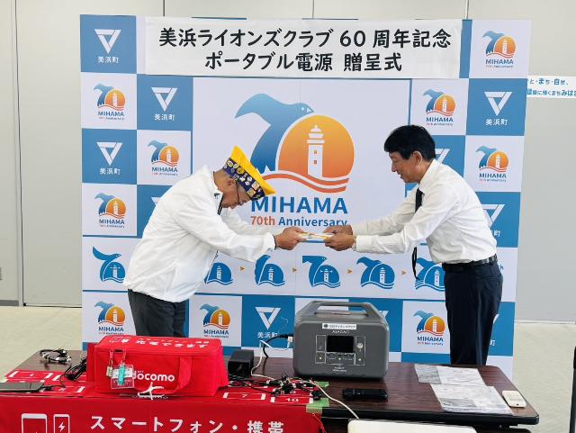 美浜ライオンズクラブ様からポータブル電源とソーラーパネルの寄附を町長が受取っている様子