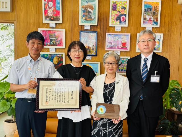 ぶっくふれんずの代表者2名と、町立図書館長、町長が賞状と写真立てを手に持って写っている様子。