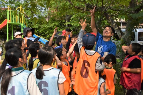 河和児童遊園で、代表者の男性を中心にゼッケンを付けた参加者の子ども達が集まり、発言をしようと手を挙げている写真