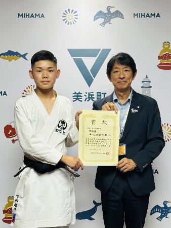 全国大会出場の報告に来庁した下岡さんと町長が、一緒に賞状を持っている様子。