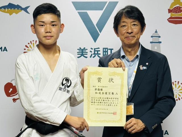 全国大会出場の報告に来庁した下岡さんと町長が、一緒に賞状を持っている様子。