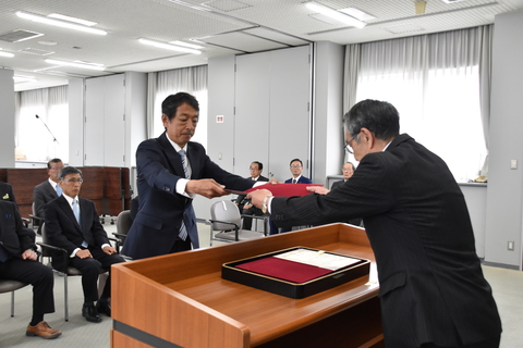 八谷さんが緊張な面持ちで山田委員長から当選書を両手で受け取っている写真