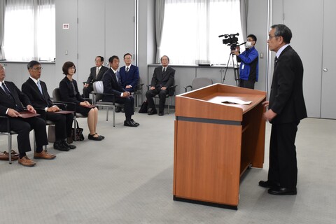 山田委員長が演台の前に立ち、選挙当選者は手を膝に置いて椅子に座っている当選証書付与式の様子の写真