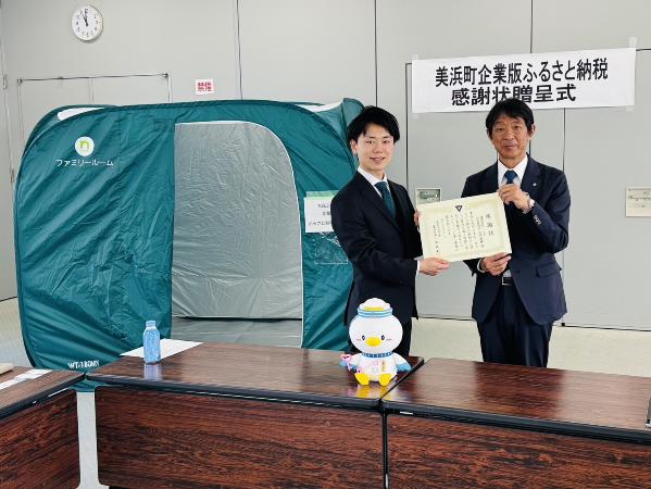 株式会社ニードの代表者と町長が感謝状を持ち、背後には寄付いただいたテントがある写真。