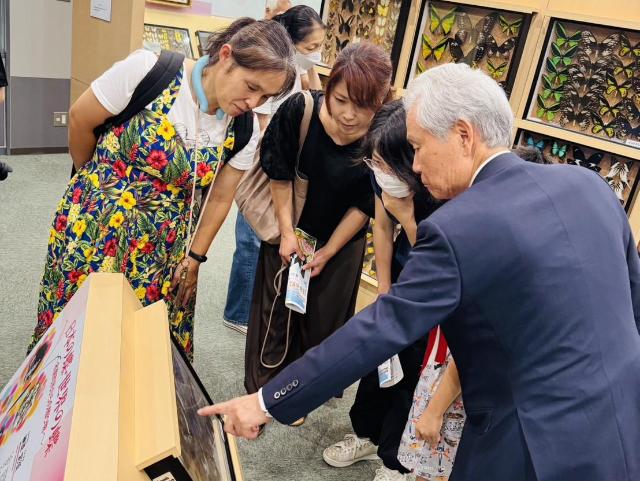 みはまバタフライミュージアムの展示室で、来場者に対し、標本に指をさしながら説明をしている榊原様の様子。