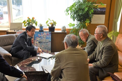 机に資料を置き、町長がジェスチャーをしながら男性3人と対話している「町長対話室」の写真