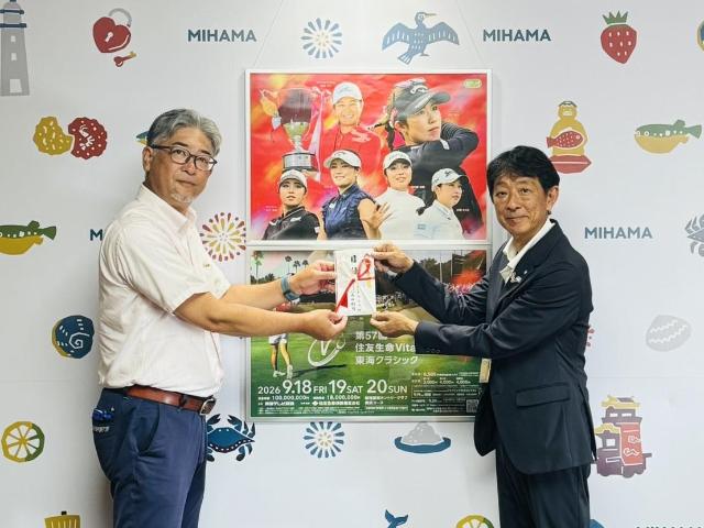 第57回住友生命vitalityレディス東海クラシックのポスターを背に、株式会社トウチュウの代表取締役社長と町長が目録を手にしている様子。