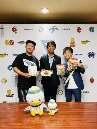 笑った！コライスの素と調理見本を持つ町長、タコライスの素を持つトマト農家の小鈴さん、愛知県住みます芸人の小鈴木さんが一緒に写っている様子