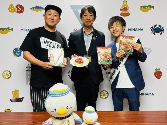 笑った！コライスの素と調理見本を持つ町長、タコライスの素を持つトマト農家の小鈴さん、愛知県住みます芸人の小鈴木さんが一緒に写っている様子