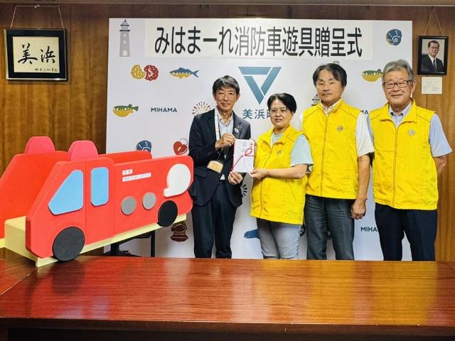 寄付いただいた消防車遊具と、美浜ライオンズクラブの3名と町長が写っている様子。