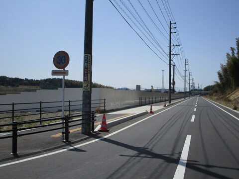 陸上競技場の建設予定地を囲むように、真っすぐに伸びた町道と歩道の左側に設置された白い鋼板塀の写真