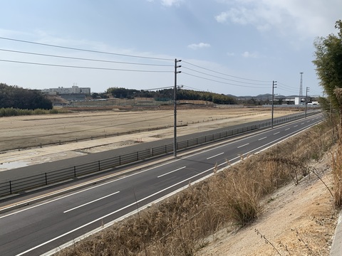 広大な陸上競技場の建設予定地と町道と歩道の横に鋼板塀が新たに設けられた様子を高台から撮影した写真