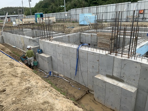 建設予定地の陸上競技場観覧スタンドの2メートルくらい窪んだ地面で、ヘルメットを被った作業員が作業を行っているコンクリートの打設工事の様子写真