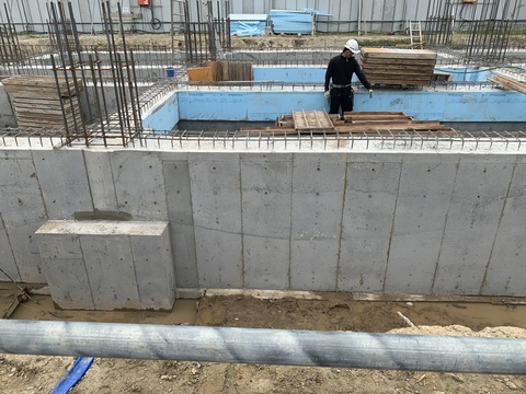 建設予定地の陸上競技場観覧スタンドの鉄筋が組まれた基礎部分にコンクリートの打設工事が行われ、ヘルメットを被った作業員が枠の中で工事を行っている様子の写真