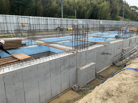 建設予定地の陸上競技場観覧スタンドに鉄筋が組まれた基礎部分で作業員がコンクリートの打設工事を行っている様子の写真