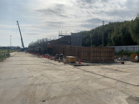 三角コーンが設置された建設現場の前に資材が置かれ、足場が組まれた陸上競技場観覧席前に、アームが延びたクレーン車が停車して工事が行われている様子の写真