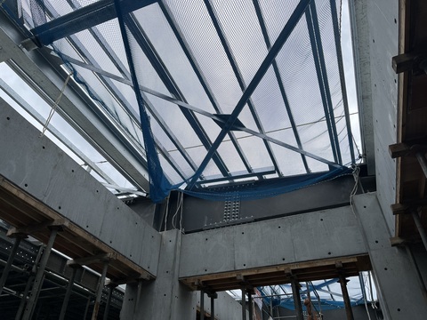 周囲や内側に足場が組まれた陸上競技場観覧スタンドの屋根部分が青色のネットで覆われている写真