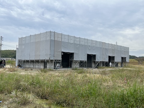 建物の周囲に足場が組まれ、4箇所の出入り口以外がネットで覆われている陸上競技場器具庫の建設中の写真