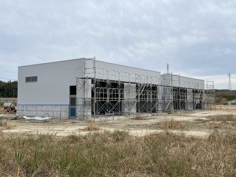 白壁に塗装された陸上競技場器具庫の左壁側の足場が解体され、正面側には足場がまだ残っている写真