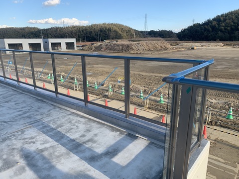 左奥に建設中の器具庫があり、手前の陸上競技場観覧スタンドにステンレス製の柵にガラスが施された手すりの写真