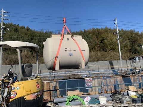 大きなクレーン車で吊るされた浄化槽を深い穴の中に下ろしている、陸上競技場の浄化槽設置工事の様子写真