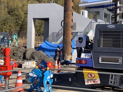 2名の作業員が位置を確認しながら慎重に照明塔の支柱を下ろしている設置工事の様子写真