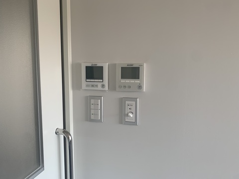 部屋の出入り口の壁側に設置された、照明のスイッチや空調設備機器のコントローラー、音響設備のスイッチを撮影した写真
