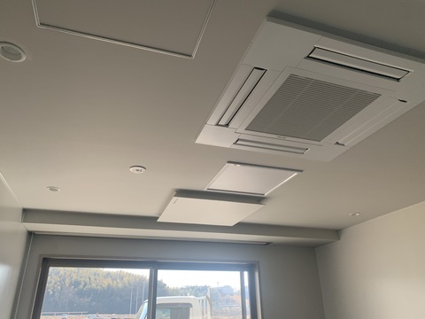奥に窓ガラスが設置された室内の、空調設備機器が設置された天井を撮影した写真