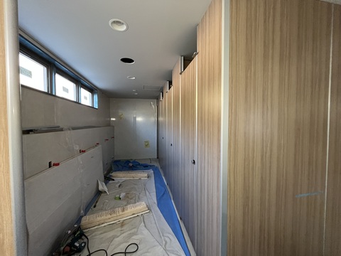 右側に木目調の仕切りや扉が施された3室のトイレの設置工事が行われている様子の写真