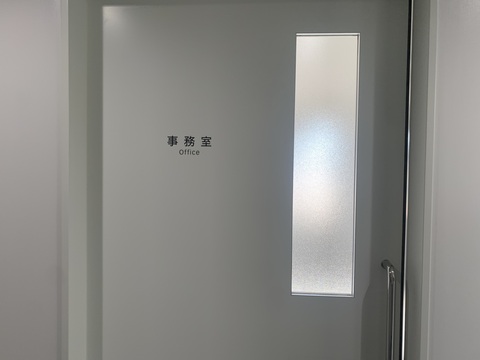 右上に縦長のすりガラスが施された引き戸の中央上部に「事務室Office」と書かれたサインが取り付けられた写真