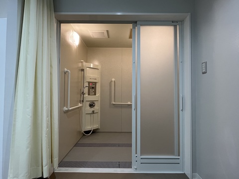 奥と左壁に手すりが設置され、左奥にシャワーが備え付けられている、車いすに乗ったまま利用できる障害者用のシャワー室内部の写真