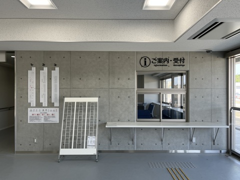 出入り口右側に「ご案内・受付」と書かれた受付台が設置され、左側の壁に1階から3階までのフロアマップと利用上の注意事項が記載されたサインが貼られ、パンフレットスタンドが設置されている観覧スタンドの入り口写真