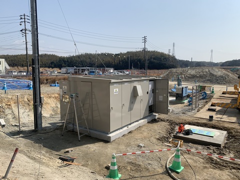 緑色の三角コーンで仕切られた、一段下がった敷地内で行われている高圧受変電設備設置工事の様子写真