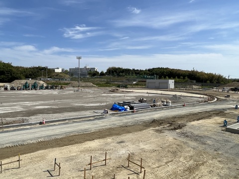 工事車両や資材が置かれているフィールドとトラックの間に等間隔で三角コーンが並び、側溝の設置工事が行われている様子を観覧スタンドから撮影した写真