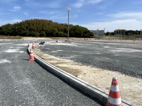 右に緩やかにカーブしたフィールド沿いに三角コーンが置かれ、トラックとフィールドの間の部分にブロックが並び側溝が設置されている工事の様子写真