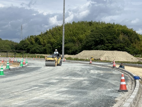 黄色のボディのロードローラに乗った作業員が、トラック部分の路床整正の工事を行っている様子の写真