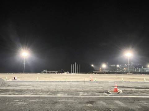 太陽が沈み夜空が広がる中、陸上競技場の左右に設置された照明塔の点灯テストが行われている写真