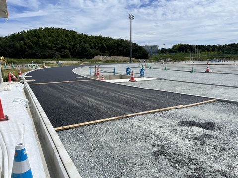 右側にカーブした路盤工事が行われたアウトフィールドの上から基層工事が行われている様子の写真